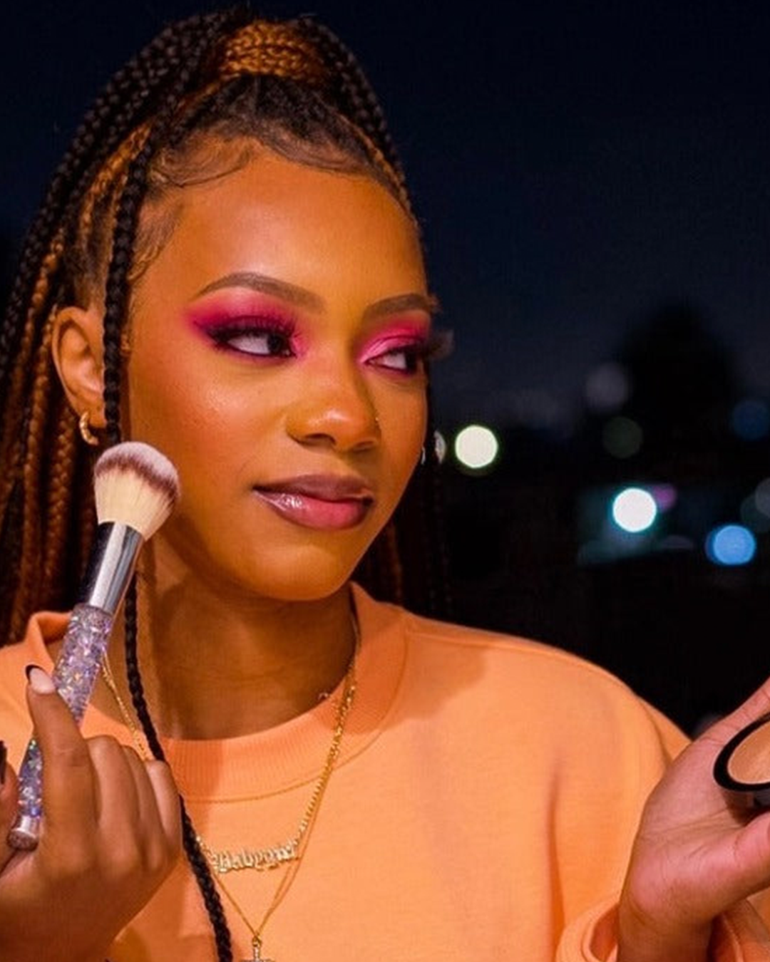 Model with creative makeup wearing shades from the Graffiti Eyeshadow Palette and applying Midtown Glow Highlighter.