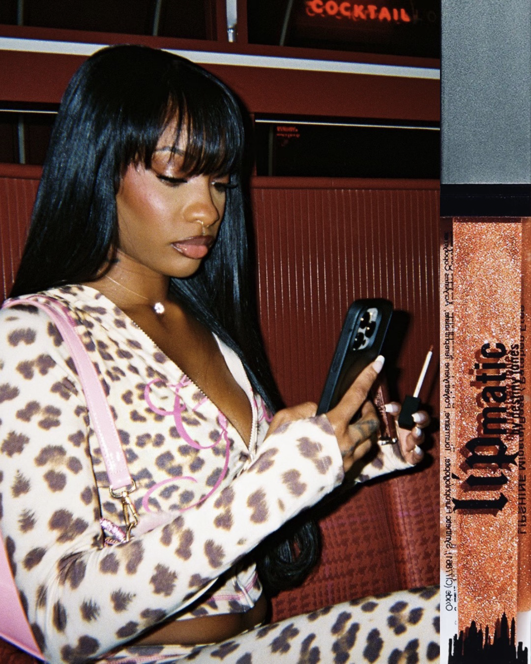 Model at a bar wearing Honey Hustle LipShine while looking at her phone.
