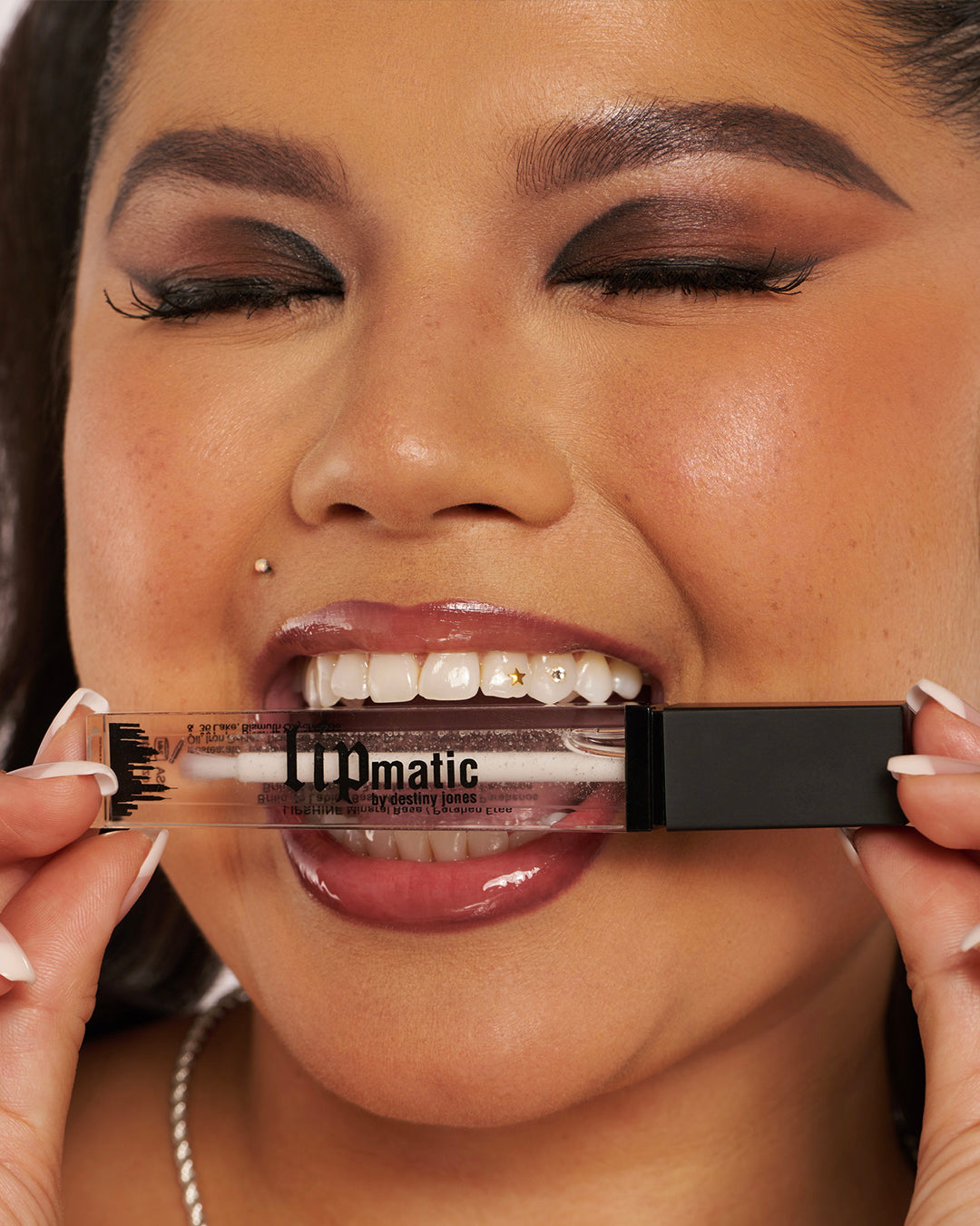 Model wearing Glaze LipShine and biting down on the Glaze LipShine tube while her eyes are closed and she is smiling.